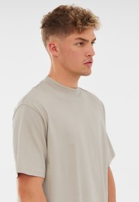 Világosszürke pamut póló kerek nyakkivágással és rövid ujjakkal, laza szabású és sima textúrájú. Nincsenek látható minták vagy fémalkatrészek.