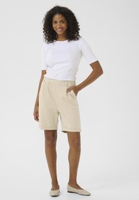 Beige op maat gemaakte shorts met opgerolde mouwen, zijzakken en een bijpassende riem, gecombineerd met een aansluitend wit T-shirt met korte mouwen.