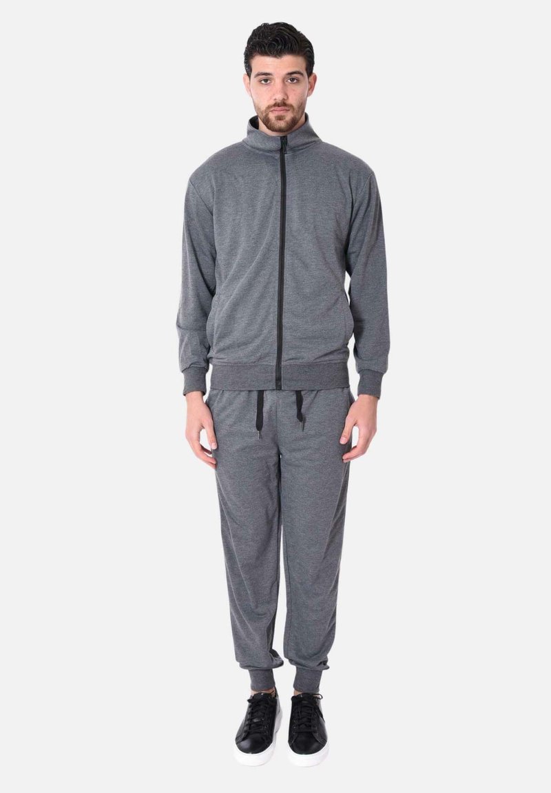 Tuta sportiva grigia composta da una giacca con zip e colletto alto e pantaloni tapered coordinati. Il tessuto ha un'aspetto morbido e testurizzato.