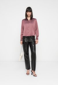 Langarm, knoopsluiting shirt in mauve satin, gecombineerd met glanzende zwarte broeken. Accessoires zijn een witte handtas en sandalen met hak in een gestreept patroon.