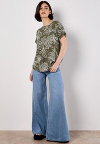 Top corto de manga corta con estampado floral verde y un ajuste relajado, combinado con jeans de pierna ancha en azul claro, con una textura desgastada y dobladillos sin terminar.
