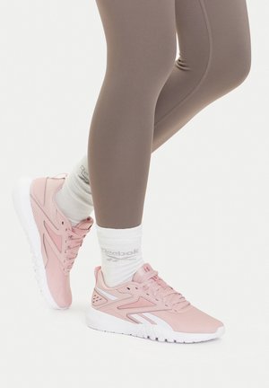 Beine in taupefarbenen Leggings, weiße Reebok-Socken und hellrosa Reebok-Sportschuhe stehend auf weißem Hintergrund.