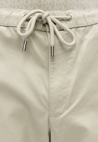 Μπεζ παντελόνι με υφή υφάσματος, διαθέτει ελαστική μέση, κλείσιμο με κορδόνι με ασημένιες άκρες και πλαϊνές τσέπες.