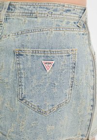 Dżinsowa mini spódnica w jasnoniebieskim kolorze z przecieranym wykończeniem, z postarzanym wyglądem i trójkątnym logo Guess na tylnej kieszeni.