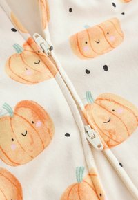 White fabric with a zipper featuring a pattern of smiling orange pumpkins with green stems and small black dots.