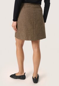 Jupe évasée en tweed marron avec une texture lisse, dotée de coutures au dos pour un ajustement. Associée à des ballerines noires à enfiler.