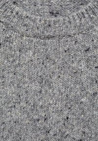 Gros plan sur un pull en laine grise tricoté, montrant un col rond côtelé et un tissu texturé avec un motif moucheté.