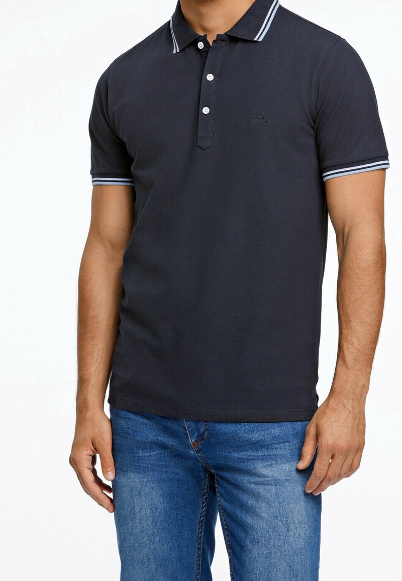 Polo marine avec des rayures contrastantes bleu clair sur le col et les manches. Dispose d'une patte de boutonnage à trois boutons et d'un logo discret.