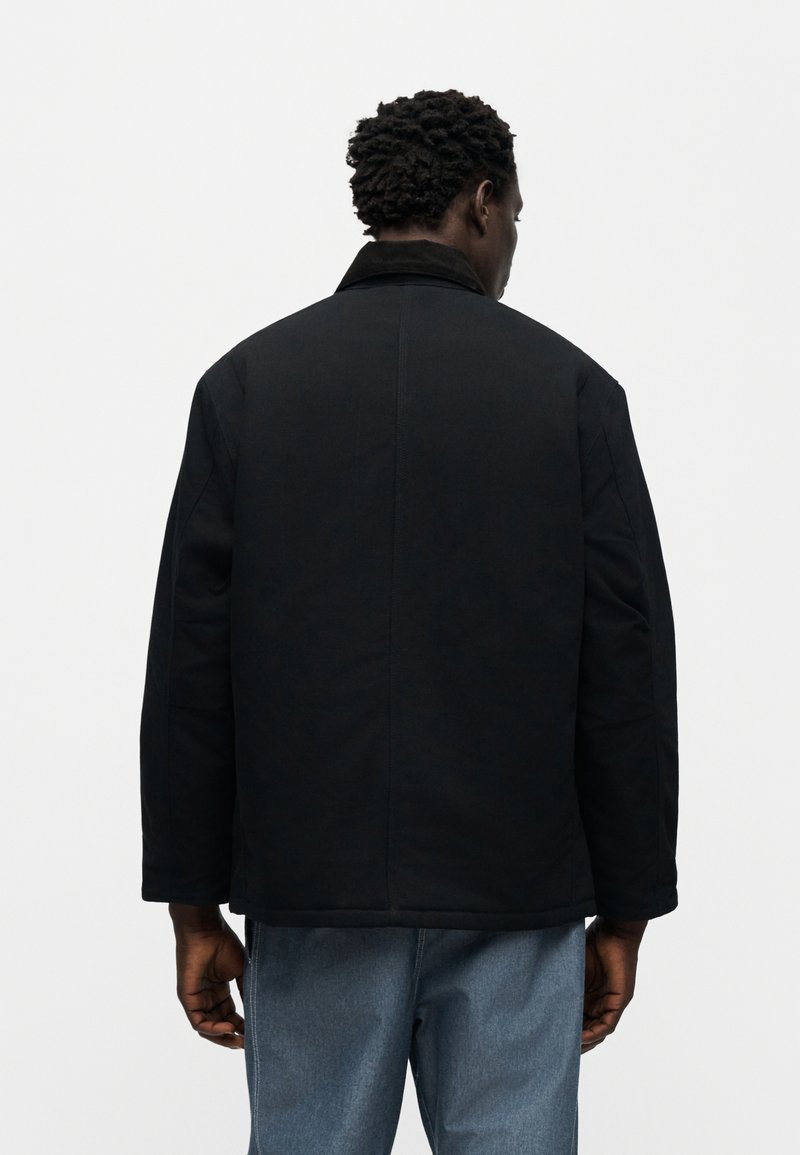 Zwarte jas met een gestructureerde silhouet, voorzien van een kraag, lange mouwen en een gladde textuur. Achteraanzicht toont minimale details.