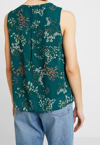 Haut sans manches en tissu vert avec un motif floral aux accents blancs et rouges. Coupe ample avec un pli au dos.