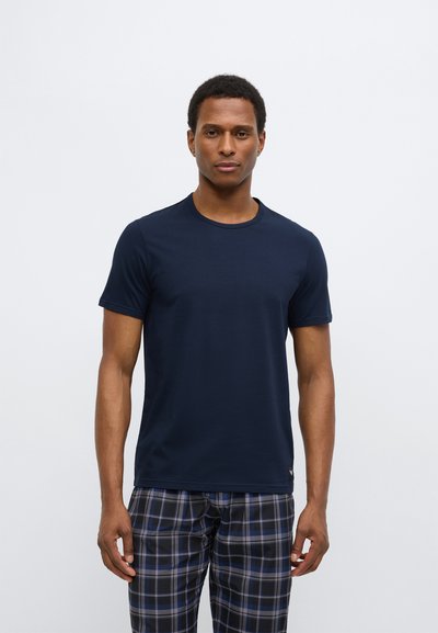 Tamsiai mėlyna trumpomis rankovėmis marškinėliai iš minkštos medžiagos su apvalia iškirpte, derinami su languotomis languotomis kelnėmis.