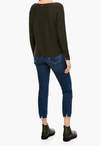 Maglione strutturato verde oliva con scollatura ampia, abbinato a jeans cropped blu scuro con orli sfrangiati e stivaletti neri con borchie.