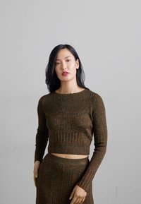 Pulover scurt, tricotat cu model de nervuri, de culoare maro, cu mâneci lungi și decolteu rotund. Finisaj texturat, asociat cu o fustă asortată.