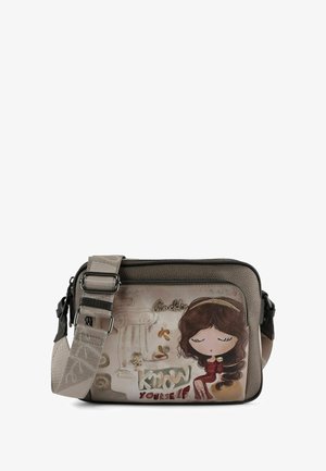 Sac bandoulière avec un extérieur taupe texturé, présentant une illustration de fille en dessin animé, des détails brodés et une bandoulière réglable.