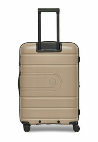 Valise rigide de couleur beige avec une surface texturée, poignée noire rétractable, quatre roues et un détail de design incurvé sur le devant.