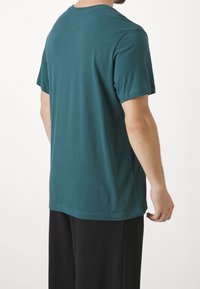 Mörkt teal-färgad bomullströja med klassisk rund halsringning och korta ärmar, med rak skärning och mjuk textur. Inga synliga mönster.