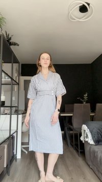 Gestreiftes Kleid mit einem Kragen zum Knöpfen, kurzen Ärmeln und einem taillierten Gürtel. Farbschema in Weiß und Marineblau. Glatte Stofftextur.