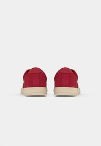 Red suede sneakers with a beige rubber sole, featuring a textured back and smooth sides, designed with minimalistic accents.