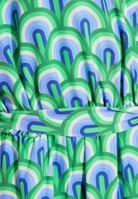 Tissu à motifs verts et bleus présentant des formes d'arcs superposées. Le matériau est léger, avec une taille froncée et des plis.