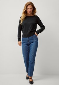 Schwarzer Strickpullover mit rundem Ausschnitt und langen Ärmeln, kombiniert mit blauen Jeans im Straight-Leg-Schnitt und schwarzen flachen Schuhen. Einfaches und lässiges Outfit.