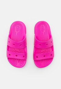 Růžové skluzavkové sandály vyrobené z pružného materiálu s dvěma širokými pásky, kruhovými otvory pro ventilaci a strukturální variantou na vnitřní straně pro lepší přilnavost.
