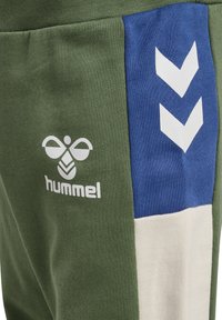 Olive green joggers with blue and white side panels, featuring white logo. Soft cotton blend with ribbed texture and chevron pattern.