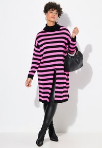 Musta ja vaaleanpunaraitainen pitkä neule, jossa on korkeakaulus ja sivuaukot, yhdistetty mustiin leggings-housuihin ja korkokenkiin. Musta käsilaukku kuuluu myös.