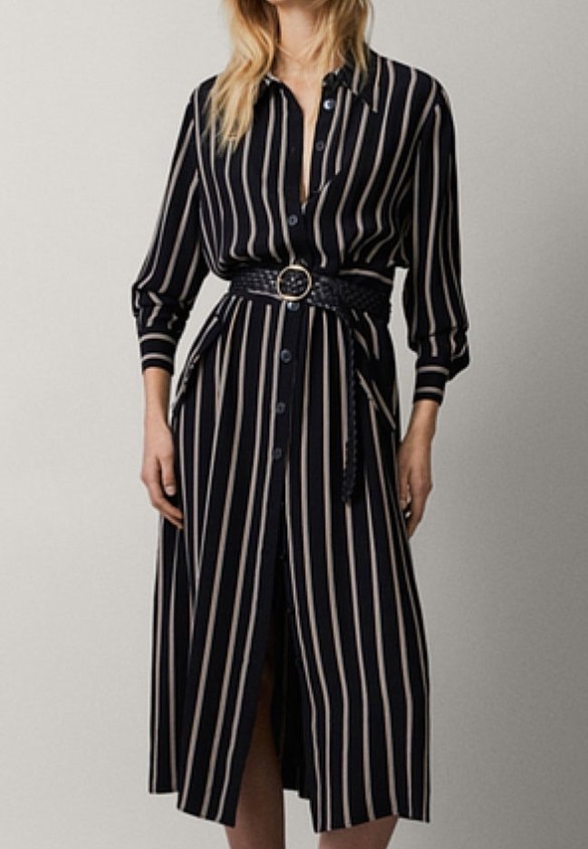 Femme portant une robe midi noire à rayures verticales beige, manches longues, boutonnée sur le devant, avec une ceinture tressée à boucle ronde.