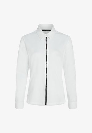 Valkoinen pitkähihaista paitaa, jossa on kaulus, musta vetoketju ja logoteippi edessä. Valmistettu pehmeästä puuvillamateriaalista.