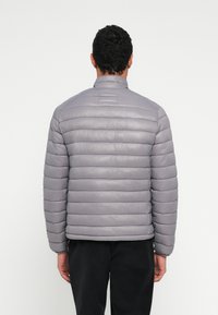 Šedá prešívaná bunda s horizontálnym prešívaným vzorom, stojacím golierom a žíhanými manžetami. Hladká textúra s ľahkým vzhľadom.