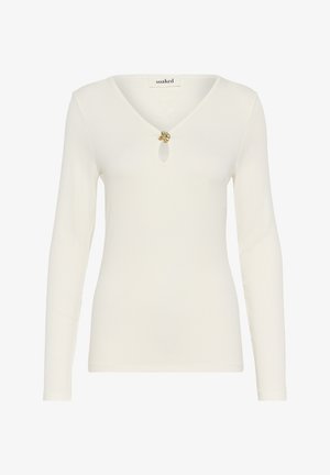 Haut à manches longues de couleur crème avec un décolleté en V et un bouton décoratif doré au niveau de la poitrine. Tissu doux et texturé.