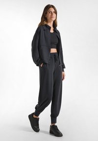 Svart kort jacka med överdimensionerade ärmar, i kombination med avslappnade svarta joggers med elastisk midja och avsmalnande mudd, samt svarta sneakers.