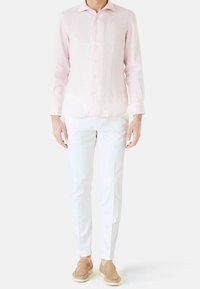 Světle růžová lněná košile s dlouhým rukávem, bílé přizpůsobené kalhoty a béžové klouzavé boty. Košile má zapínání na knoflíky a klasický límec.