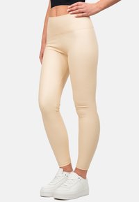 Leggings beige con vita alta e materiale liscio ed elasticizzato, abbinati a sneaker bianche. Linee pulite e design aderente.