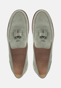 Groene suède instappers met kwastjesdetail, ronde vorm, contrasterende stiksels en een glad leren interieur. Platte zool met minimale accenten.