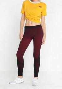 Žluté zkrácené tričko s kapsou, v kombinaci s černými a burgundskými texturovanými legínami a bílými sportovními botami.