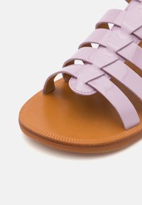Lavendel patent lær sandal med vævet stropdesign og en brun tekstureret sål. Flad form og åben tå-stil for åndbarhed.
