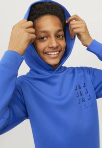 Modrá mikina s hladkou texturou, má velkou kapuci a potištěný černý text na přední straně. Rukávy jsou žebrované na manžetách.