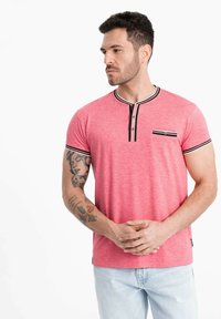 Lyserød meleret T-shirt med rund hals, vandrette sorte og hvide striber, to-knaps placket og en brystlomme. Materiale i bomuldsblanding.