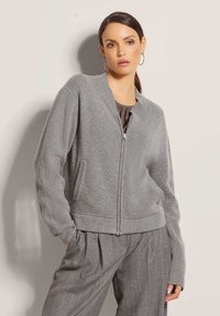 Grau gestrickte Bomberjacke mit durchgehendem Reißverschluss, gerippten Bündchen und Saum sowie seitlichen Taschen. Die Textur ist weich und hat eine lockere Passform.