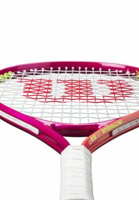 Raquette de tennis avec un cadre rose, un tamis blanc et des accents rouges. Elle possède une prise texturée blanche et un logo distinctif sur le col.
