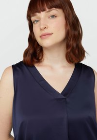 Top senza maniche blu navy realizzato in tessuto liscio, caratterizzato da un design con scollatura a V, una leggera caduta e dettagli di cucitura minimi.