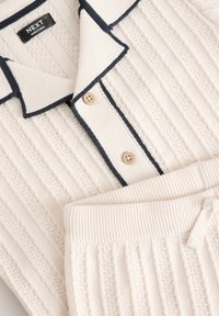 Ribstrikket lounge-sæt i creme, med en top med krave og navy kant samt to knapper, kombineret med matchende bukser med elastisk talje.