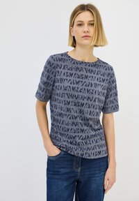 Camisa de manga corta de color azul marino con un patrón texturizado en diferentes tonalidades, cuello redondo, tela suave y corte relajado. Combinada con jeans azules.
