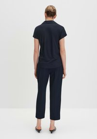 Polo bleu marine à manches courtes avec col, associé à un pantalon droit bleu marine. Tissu lisse avec une coupe décontractée. Les chaussures présentent un petit talon.