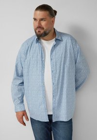 Lichtblauw overhemd met lange mouwen en een klein bloemenpatroon, met knoopsluiting aan de voorkant en een casual pasvorm, gecombineerd met een wit T-shirt eronder.