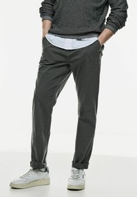 Grå raka byxor i mjukt material, tillsammans med en vit skjorta med krage och vita sneakers, med uppvikta ärmslut synliga.