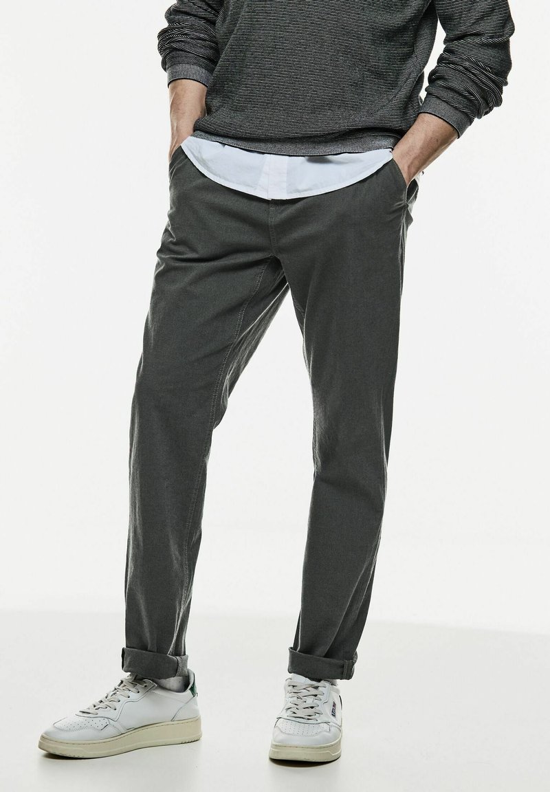 Grå raka byxor i mjukt material, tillsammans med en vit skjorta med krage och vita sneakers, med uppvikta ärmslut synliga.