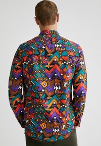 Camicia a maniche lunghe con motivo caratterizzato da vivaci forme geometriche in arancione, viola, verde e nero su una base marrone. Materiale morbido con polsini a bottoni.