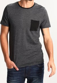 Svart och grårandig t-shirt med kort ärm som har en enfärgad svart bröstficka. Tyget ser mjukt ut och har en avslappnad passform.